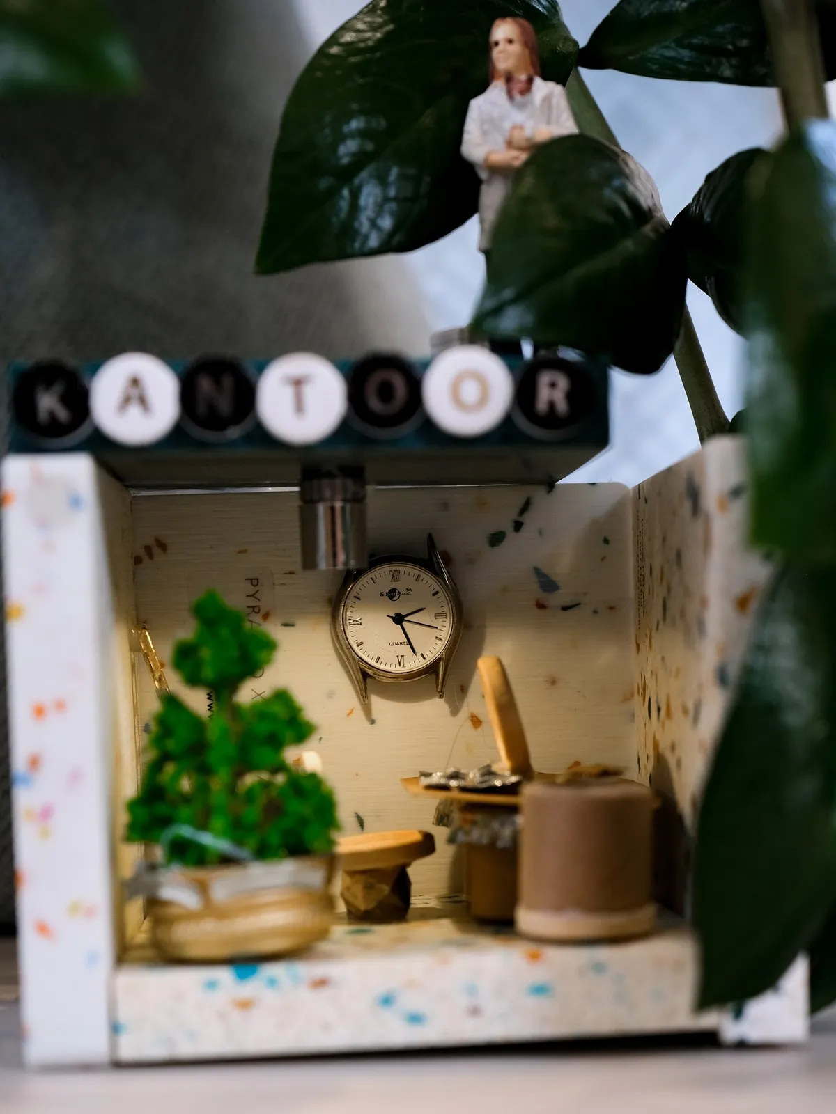 Een miniatuurkantoor met klok en plant, verstopt tussen de boeken