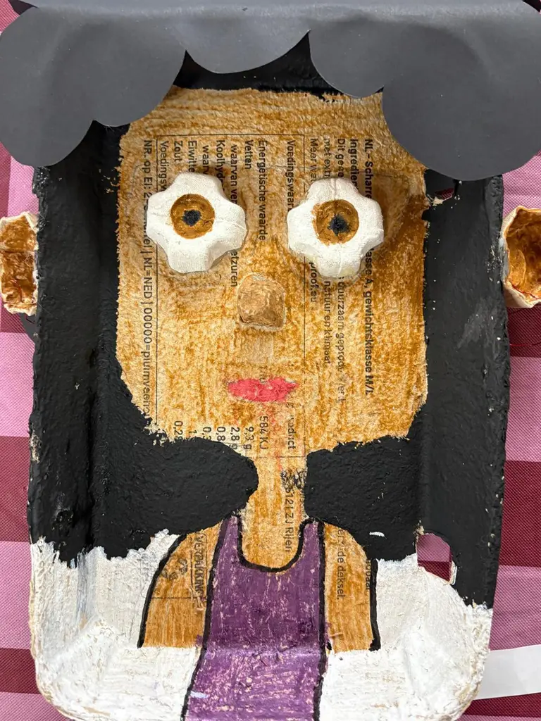 Een groot geschilderd kartonnen portret van een meisje met zwart haar en wiebelogen.