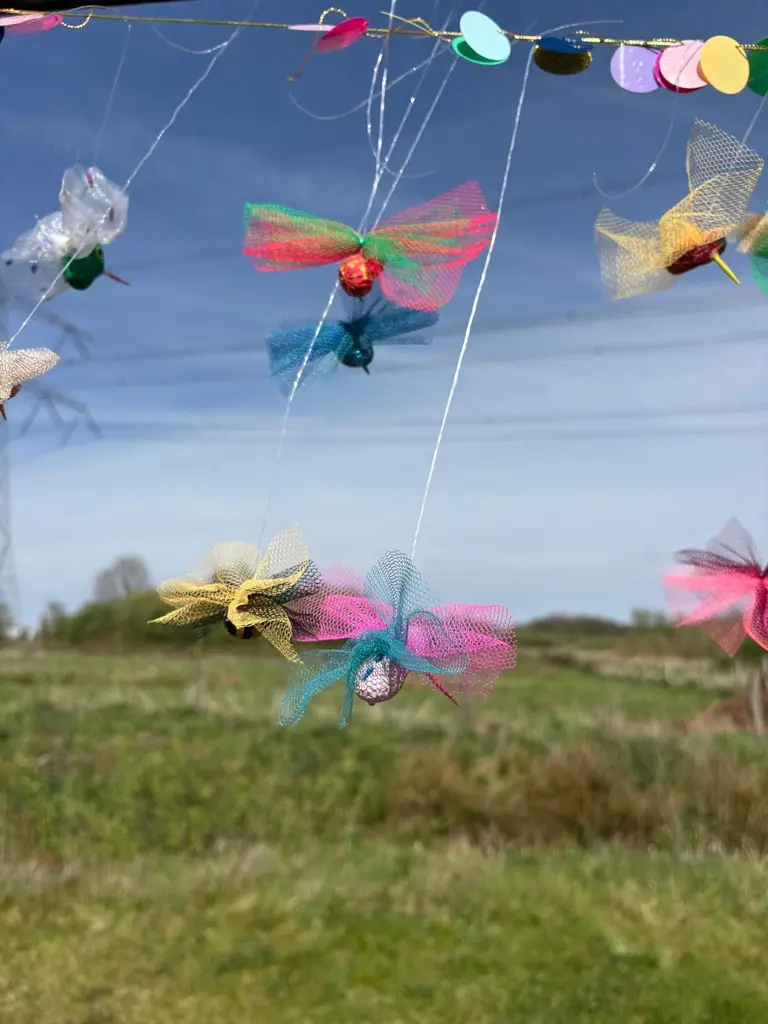 Zelfgemaakte libelles van gekleurd vliegerpapier hangen aan een draad in een weiland.
