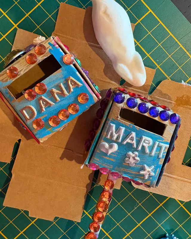 Kartonnen doosjes versierd met glittersteentjes en de namen Dana en Marit.