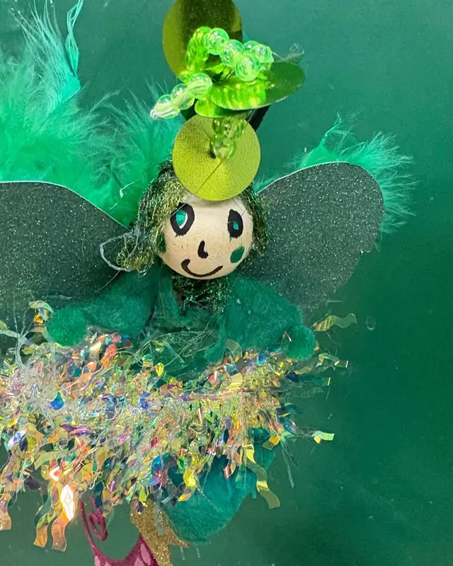 Een groen feeënpoppetje van papier, veren en glittergaren.