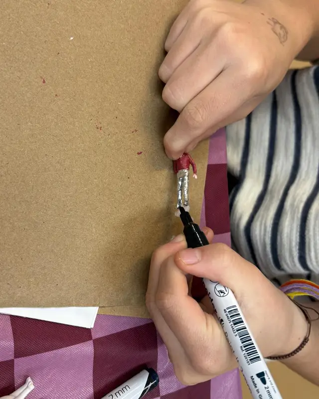 Twee handen schrijven met een zwarte stift op karton.